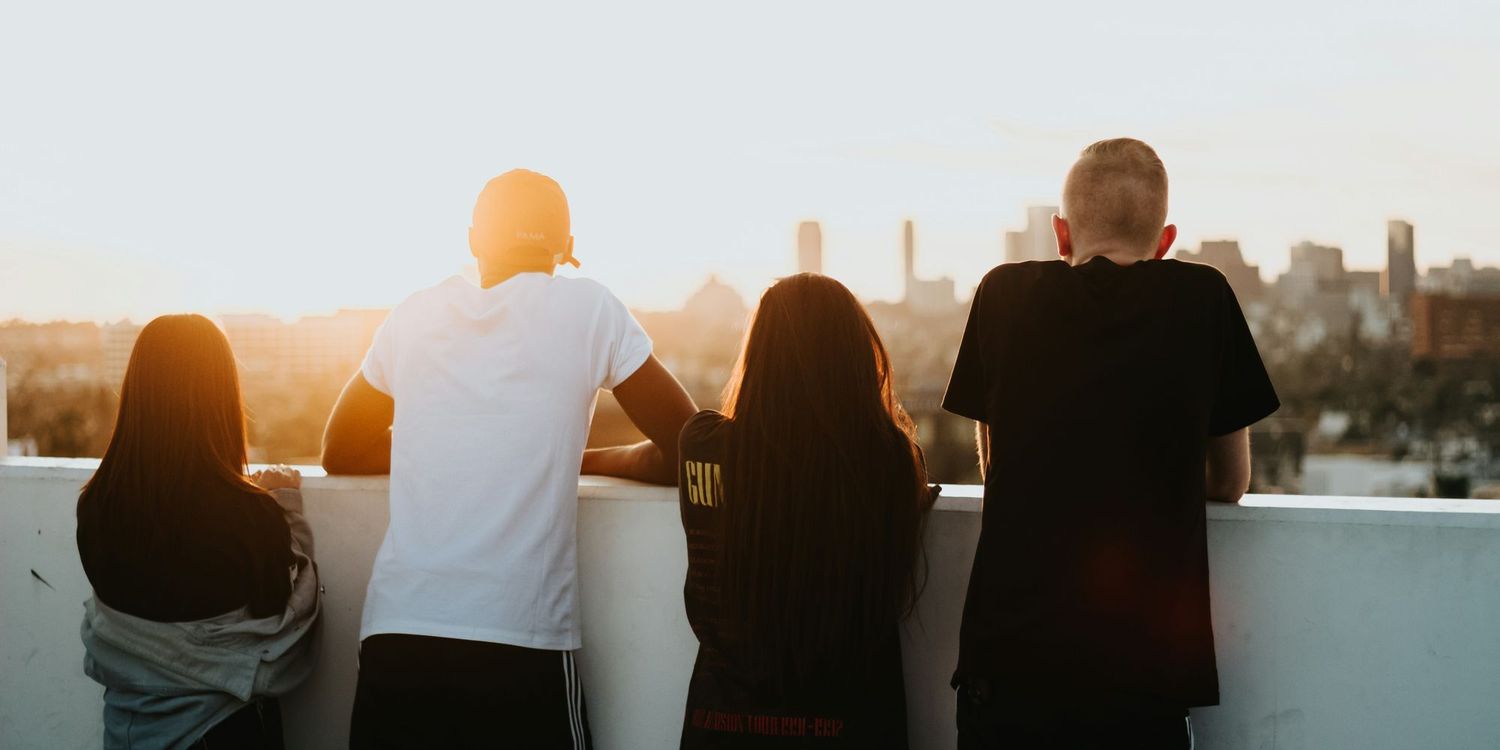 Four young people looking over at the cityscape from a tall building as the sun sets