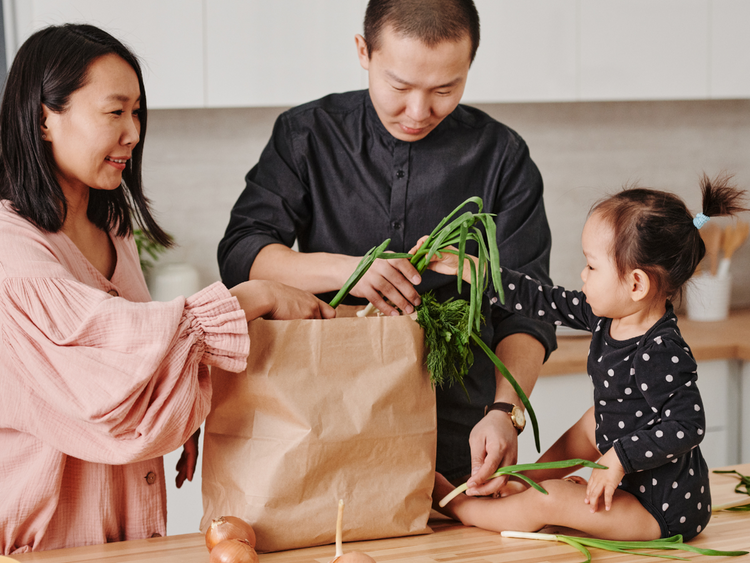 A man and a woman with a baby taking vegetables out of a paper shopping bag