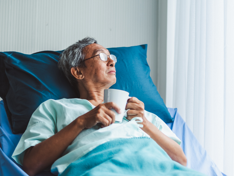 A man in a hospital bed holding a mug looking out a window